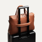 Attaché case camel en cuir pleine fleur, fixé sur une valise grâce à un passant trolley.