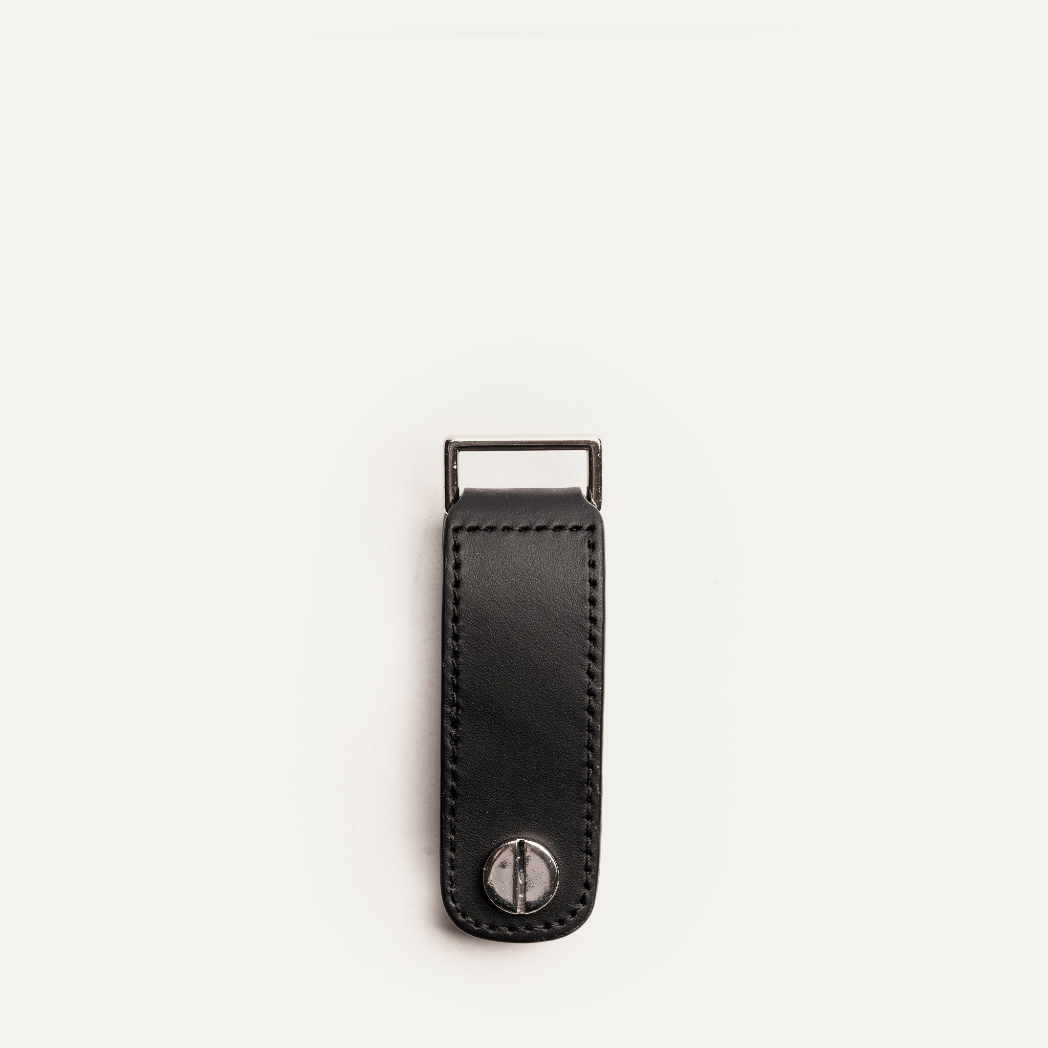 Porte clé vu de dos, montrant une vis de fixation en laiton sur cuir noir avec boucle métallique.