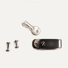 Porte clef cuir démonté avec vis, clés détachées en laiton et étui ouvert sur fond clair.