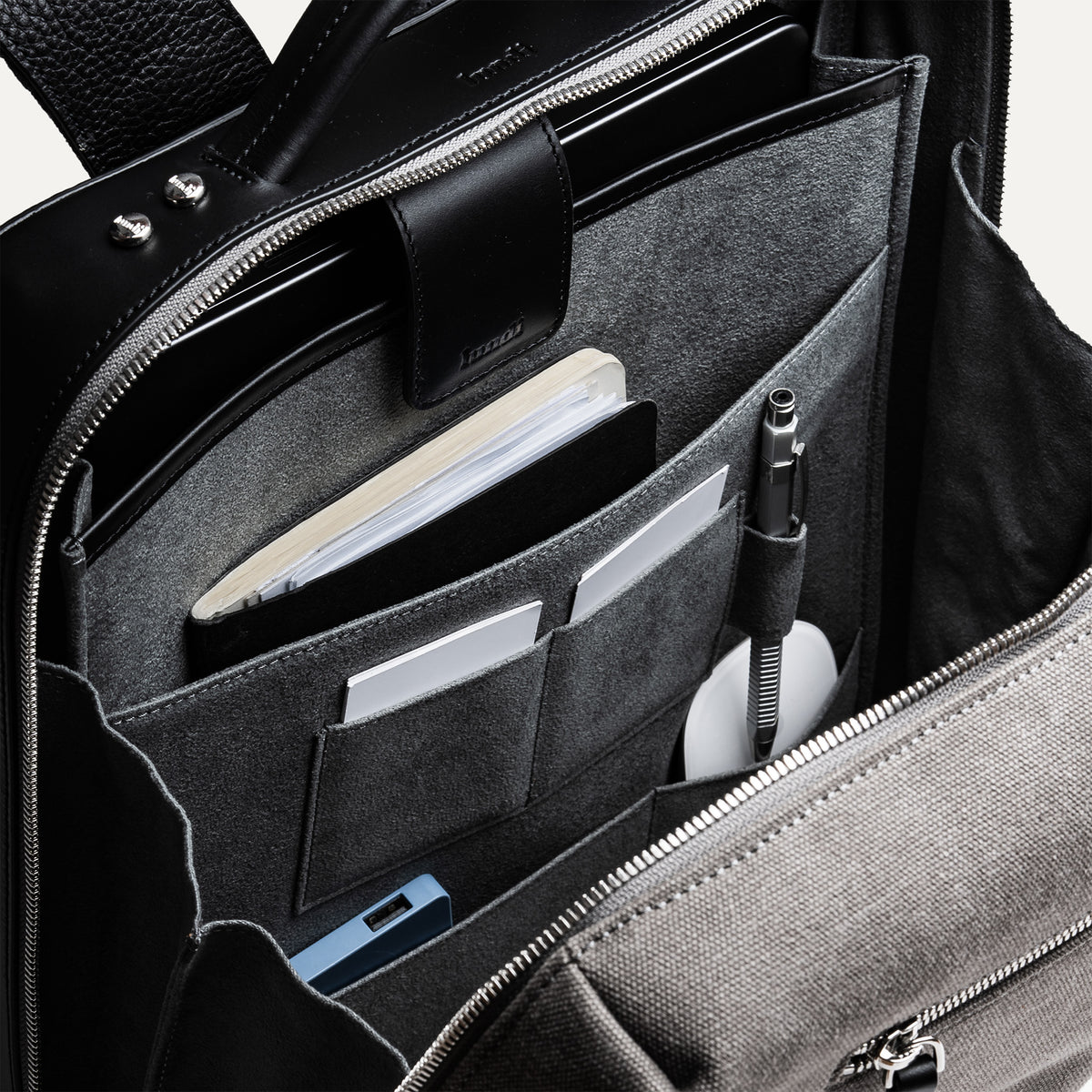 sac à dos homme en cuir et toile grise avec poches tech, stylos, carnet et rangement ordinateur.