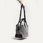Sac de voyage homme toile grise et cuir noir porté à l’épaule grâce à sa bandoulière amovible.