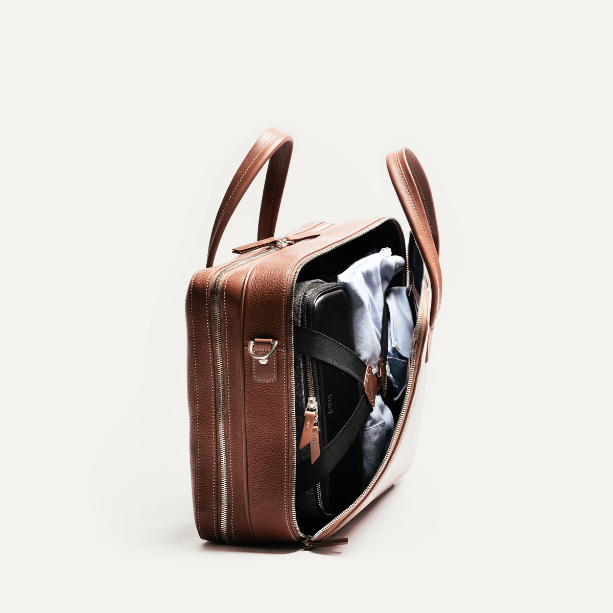 ce porte document TILIO II en cuir cognac offre deux compartiments spacieux sont parfaits pour des voyages de courte durée, permettant de transporter ordinateur, vêtements et accessoires. 
