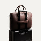 Sac à bandoulière homme fixé à une valise trolley grâce à sa bande arrière, pratique pour les déplacements professionnels.